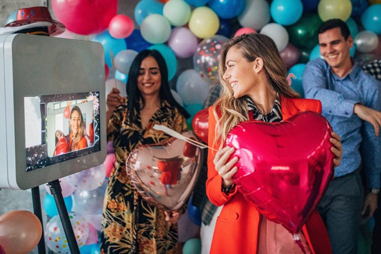 Femme Tenant un Ballon en Forme de Cœur et S'amusant devant une Borne à Selfie - Photobooth